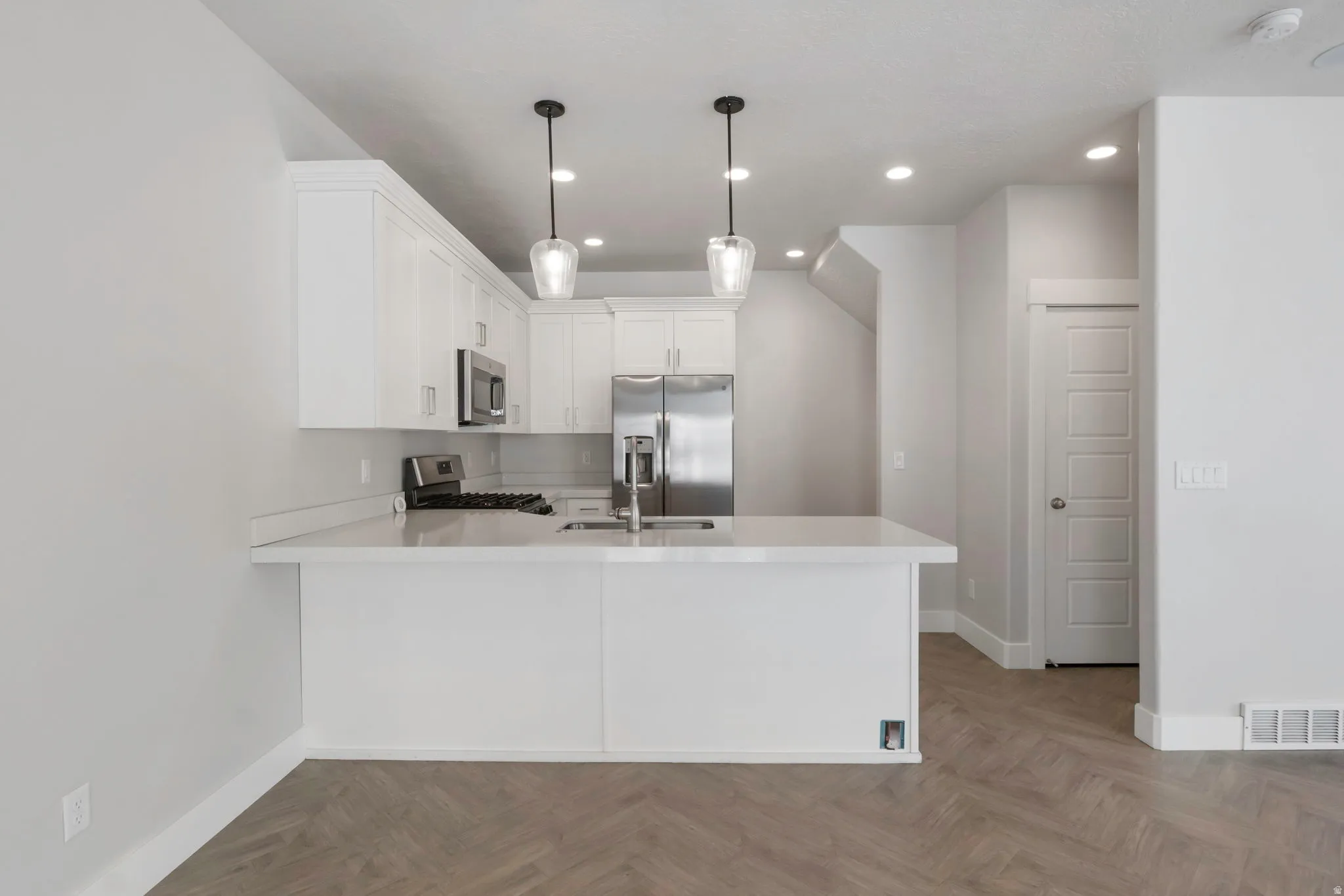 Modern kitchen featuring white shaker cabinetry, stainless steel appliances, a white solid-surface countertop, and pendant lighting