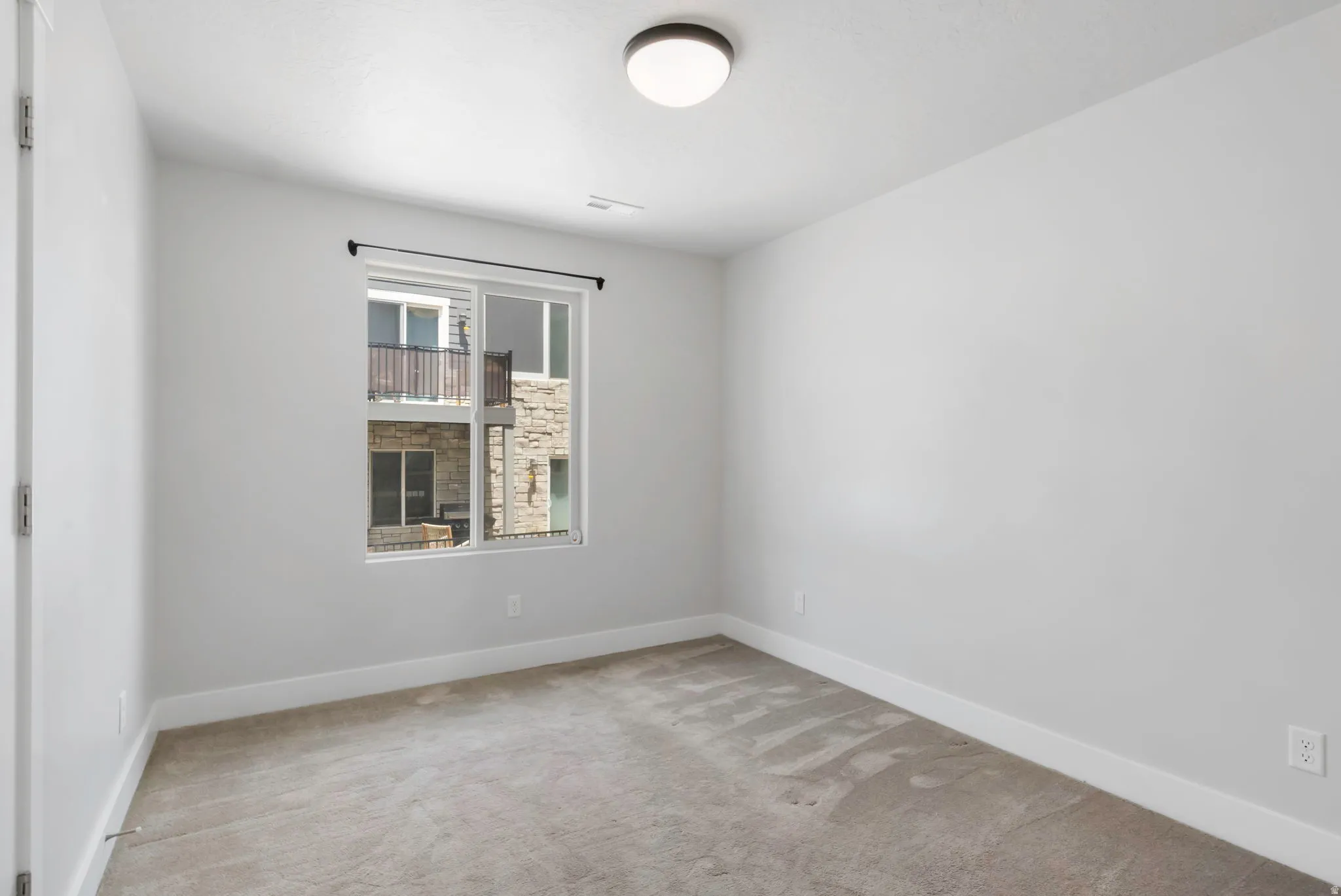 Neutral-toned bedroom featuring a single window, overhead flush-mount lighting, light gray carpeting, and white baseboards