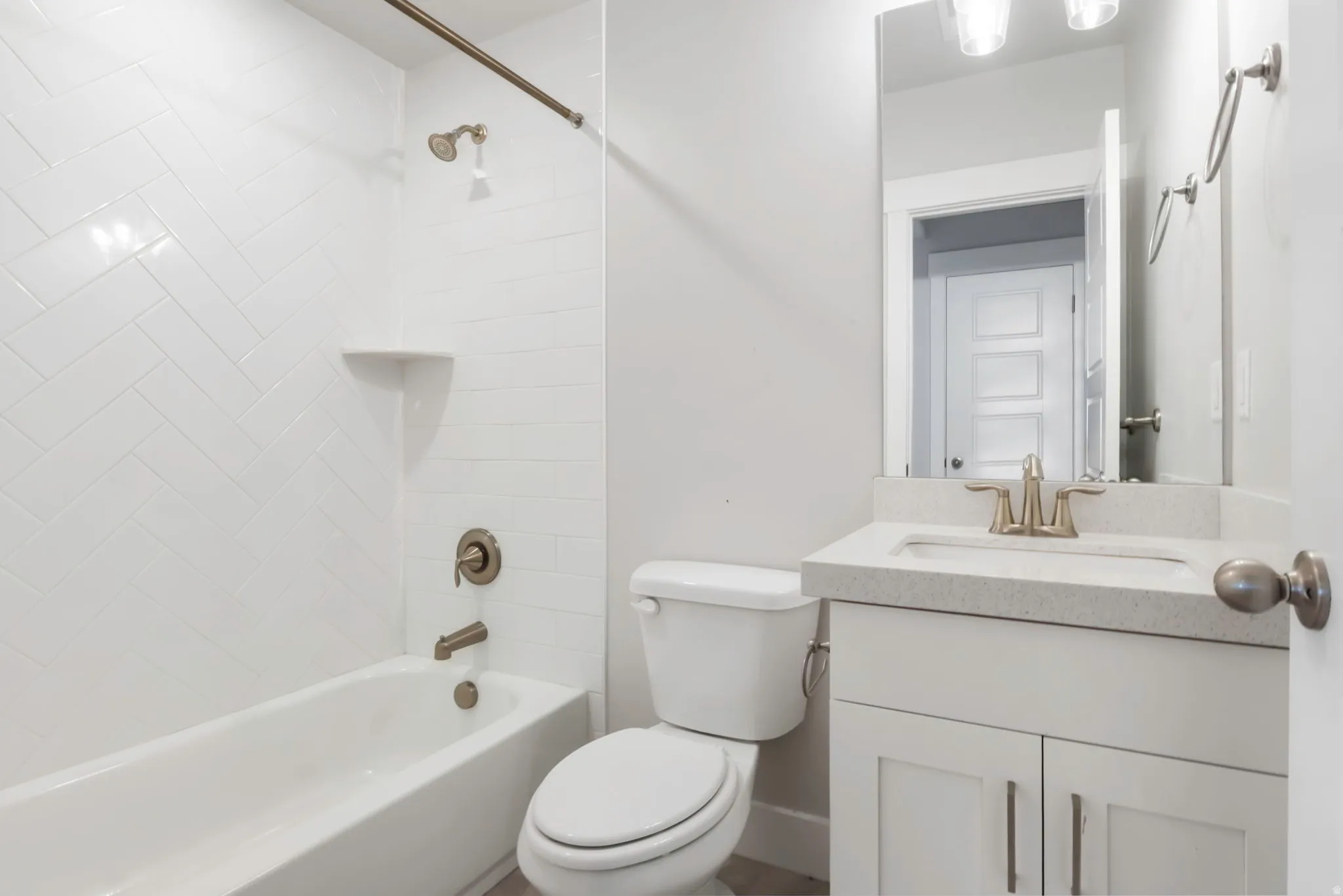Bright bathroom featuring a white subway tile surround in a herringbone pattern, a white bathtub, a toilet, a vanity with a light-colored countertop and an integrated sink, and bronze-finish fixtures