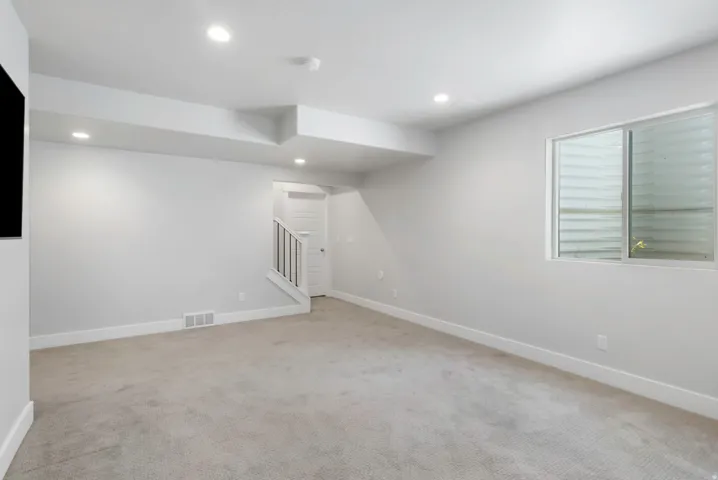 Spacious carpeted room featuring recessed lighting, a neutral color palette, white baseboards, and a window with horizontal blinds
