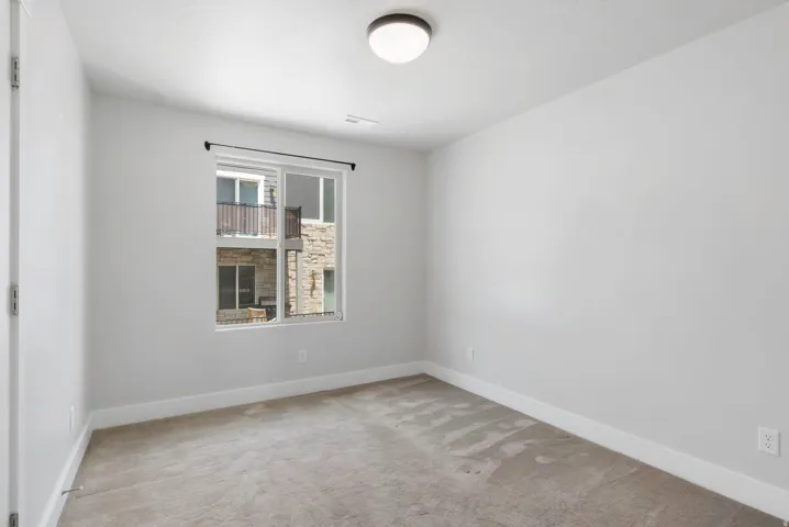 Neutral-toned bedroom featuring a single window, overhead flush-mount lighting, light gray carpeting, and white baseboards