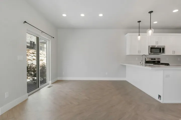Open-concept interior featuring light wood-finish herringbone flooring, a white kitchen island with a stainless steel sink and faucet, white cabinetry, recessed lighting, and a sliding glass door