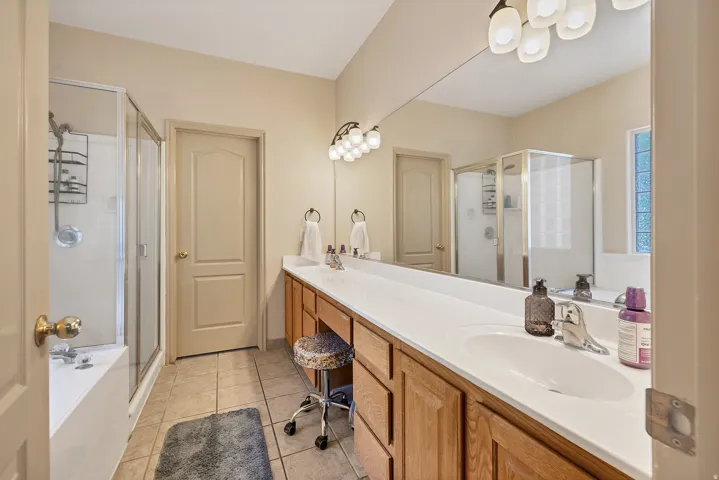 Full bath with double vanity, a shower stall, light tile patterned floors, and a garden tub