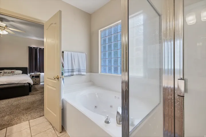 Ensuite bathroom with light colored carpet, a tub with jets, light tile patterned floors, and a ceiling fan