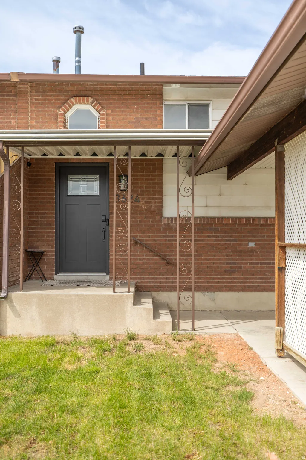View of exterior entry featuring brick siding, covered porch, and a yard