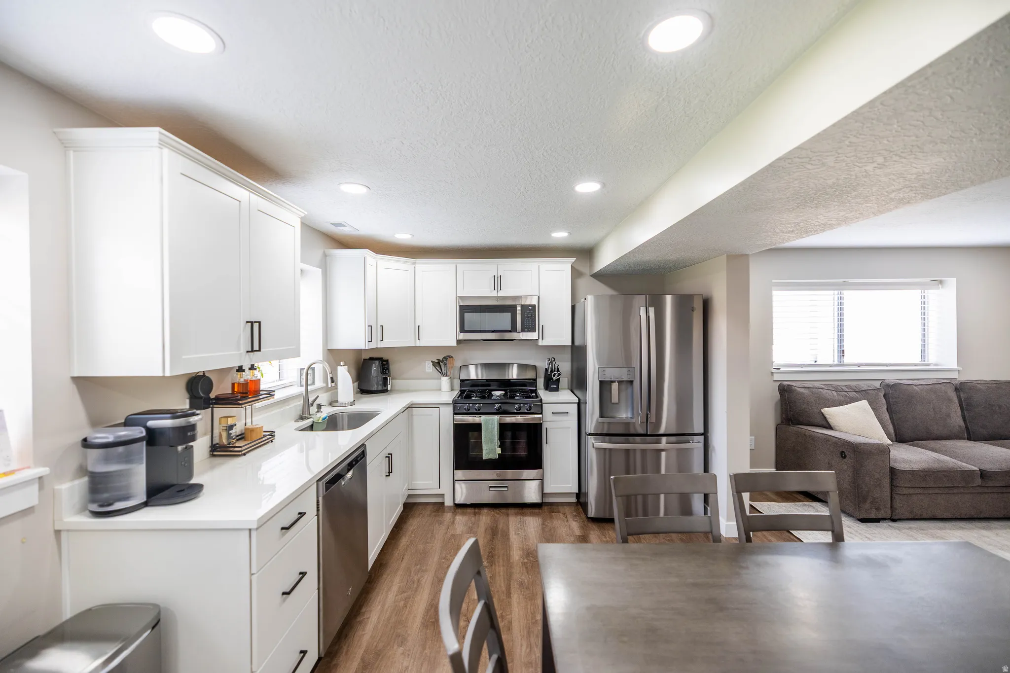 Kitchen with stainless steel appliances, white cabinetry, light wood finished floors, a textured ceiling, and light stone countertops