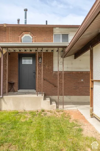 View of exterior entry featuring brick siding, covered porch, and a yard