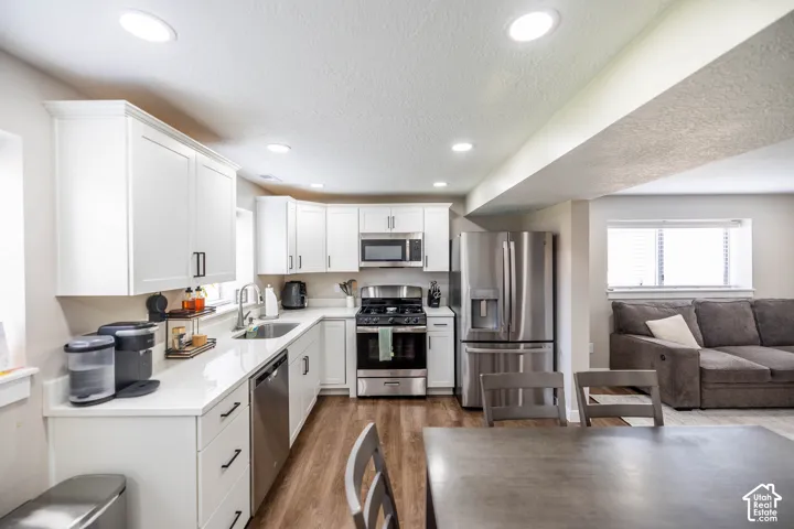 Kitchen with stainless steel appliances, white cabinetry, light wood finished floors, a textured ceiling, and light stone countertops