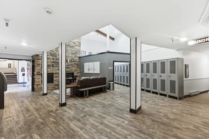 Spacious common area featuring wood-finish flooring, a stone accent wall with a built-in fireplace, and a high vaulted ceiling