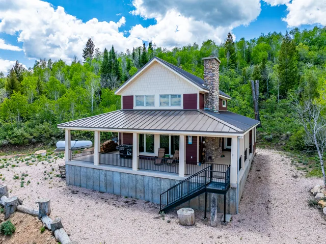 Contemporary residence featuring a metal roof, prominent stone chimney, and a covered wraparound porch with black railing