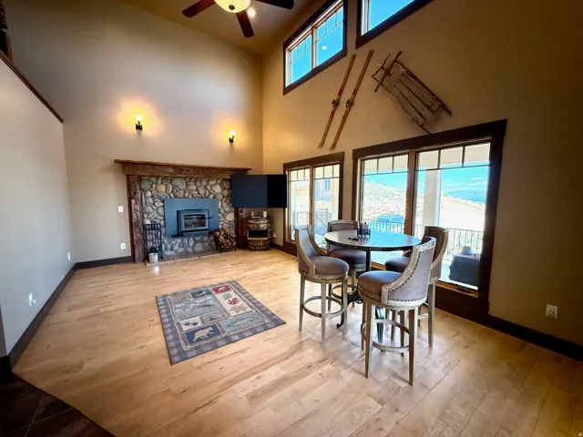 Open family room/Dining space with ceiling fan, light wood finished floors, a stone fireplace, and a high ceiling