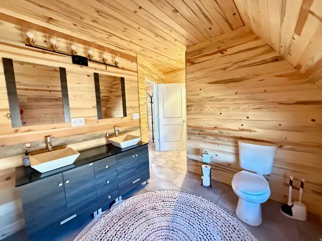Primary bathroom featuring wood walls, a vaulted wood ceiling, light tile patterned floors, and double vanity