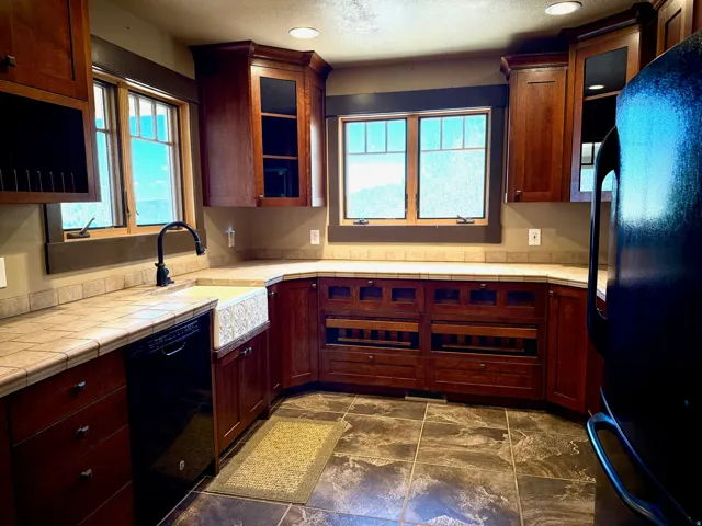 Kitchen with black appliances, tile counters, glass insert cabinets, recessed lighting, and healthy amount of natural light