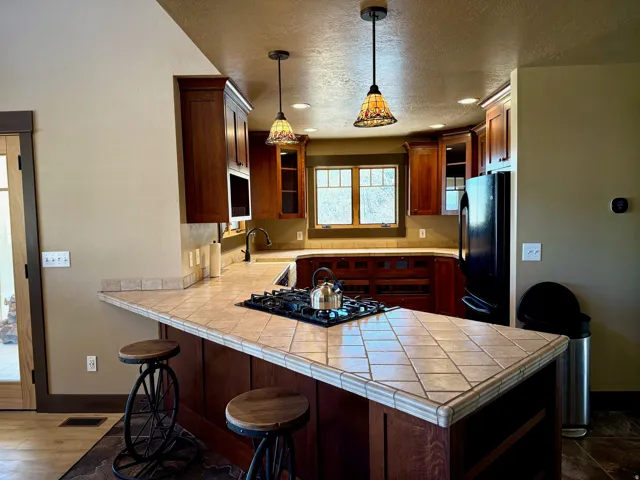 Kitchen with a peninsula, black appliances, hanging light fixtures, a breakfast bar area, and open shelves