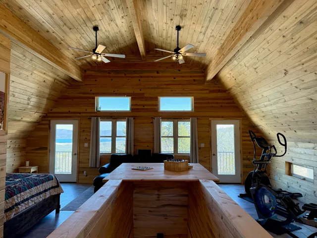 Loft bedroom/family room above detached garage with access to outside, a wood ceiling with exposed beams, wood walls, multiple windows, and a ceiling fan
