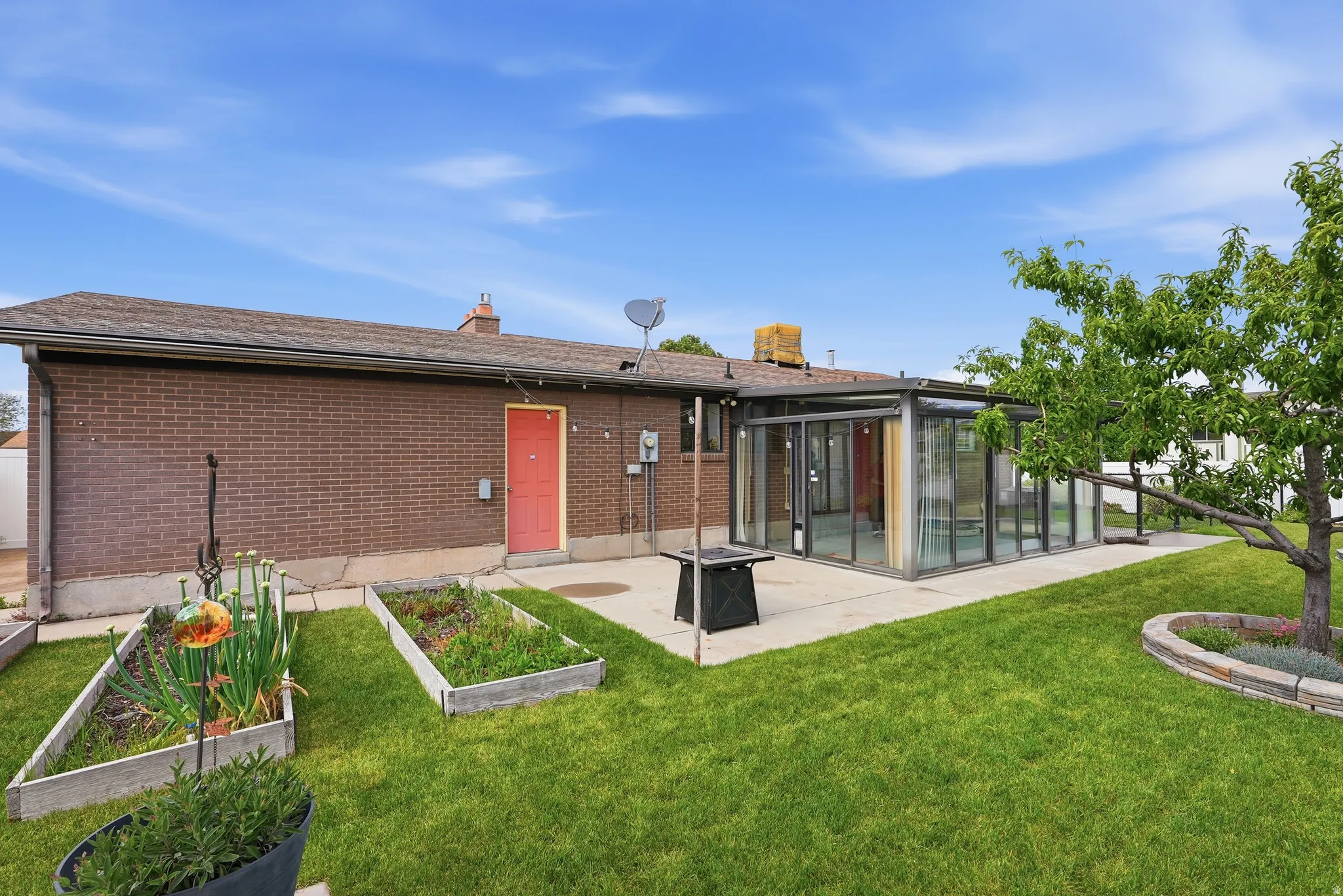 Expansive backyard featuring a lush lawn, mature tree with stone-edged planter, and raised garden beds