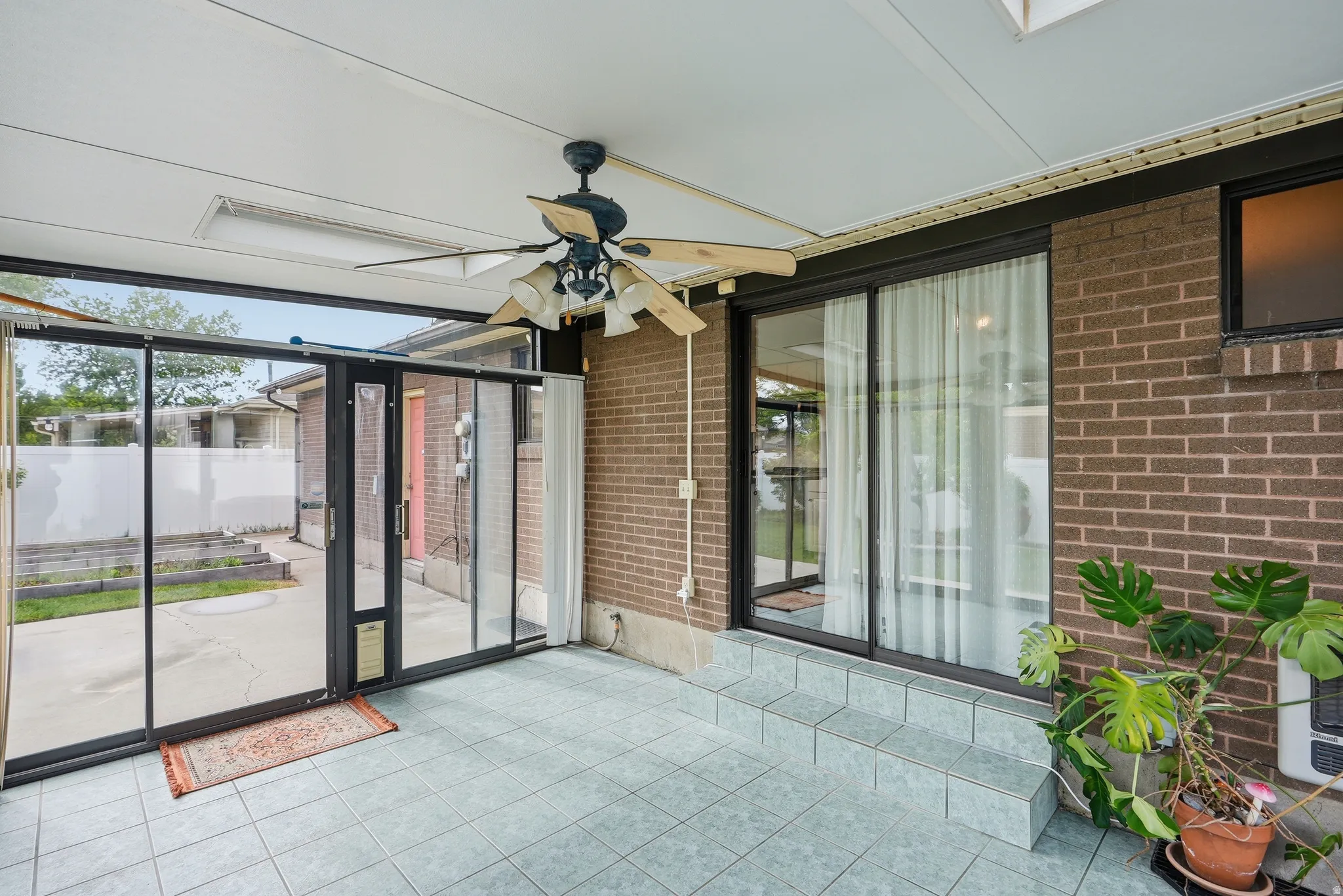 Covered patio area featuring a ceiling fan, light blue tile flooring, and multiple sliding glass doors