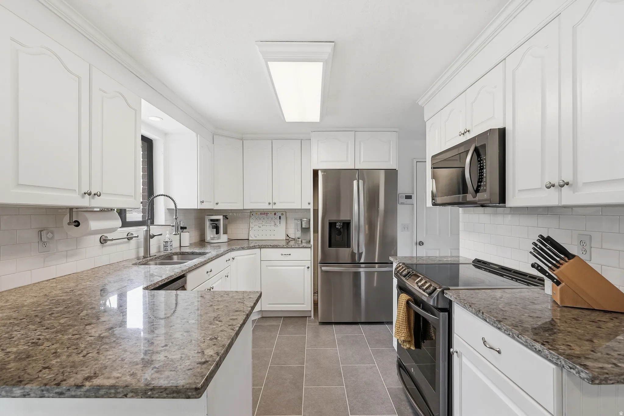 Kitchen featuring white cabinetry with crown molding, stone countertops, a subway tile backsplash, stainless steel appliances, and tile flooring