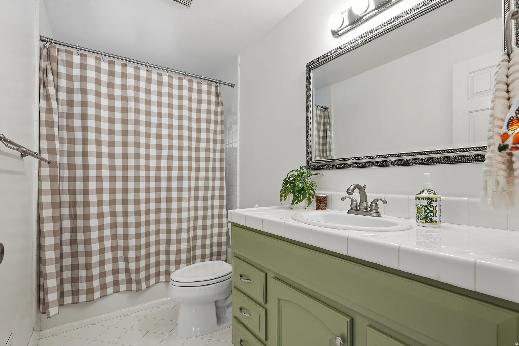 Bathroom featuring a green vanity with an integrated sink, tiled countertop, framed mirror, and a shower-over-tub combination