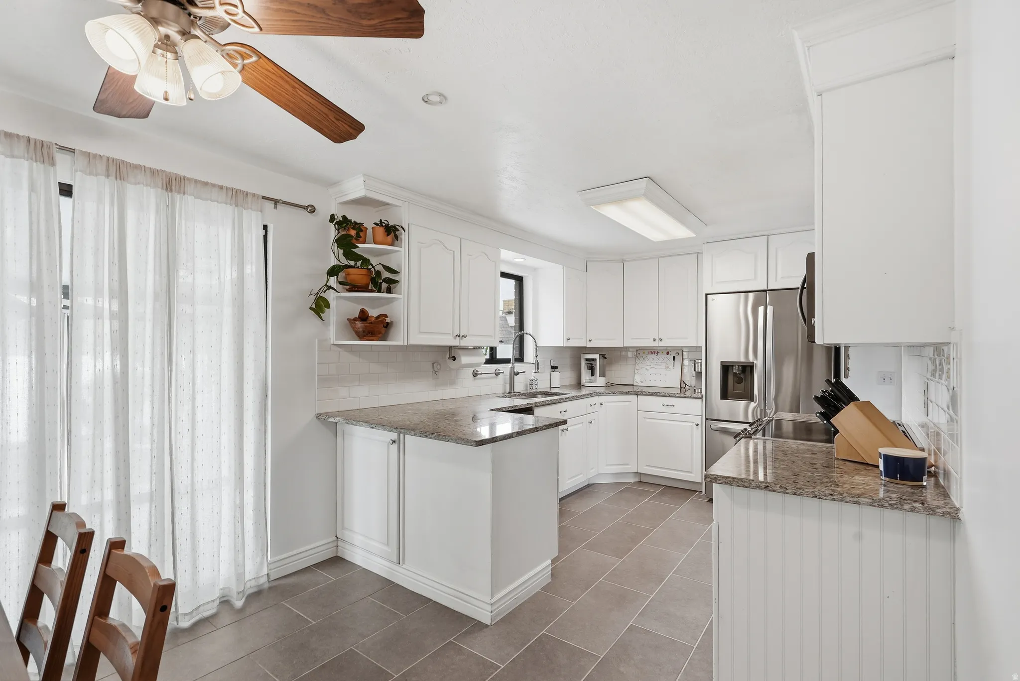 White cabinetry with crown molding, granite countertops, tile backsplash, stainless steel refrigerator, and tile flooring