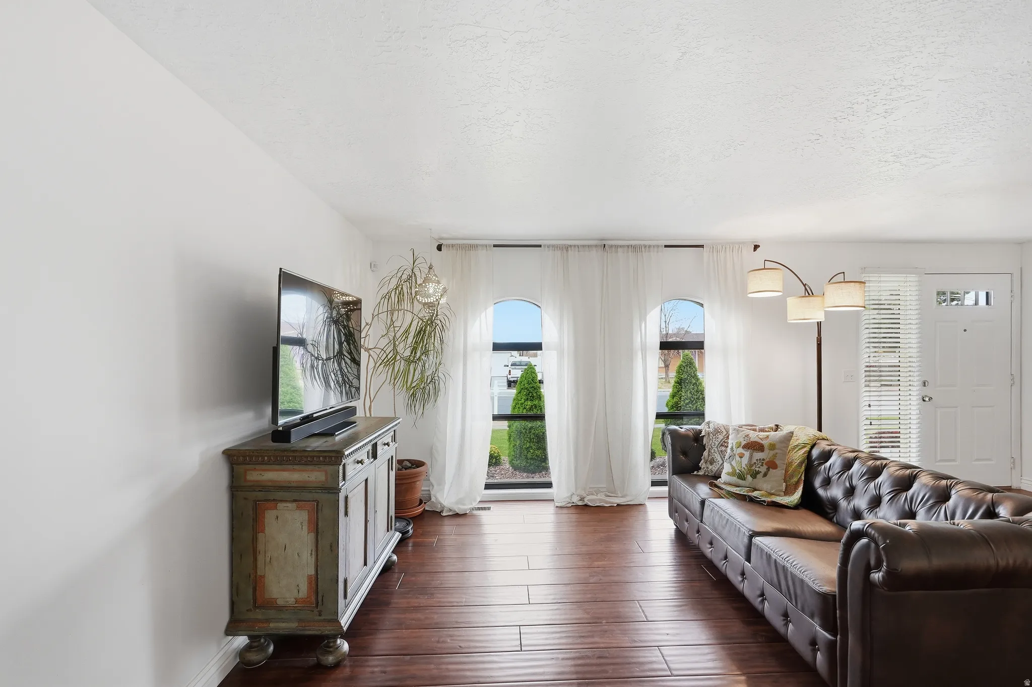 Living area featuring wood-finish flooring, white painted walls, and three arched windows