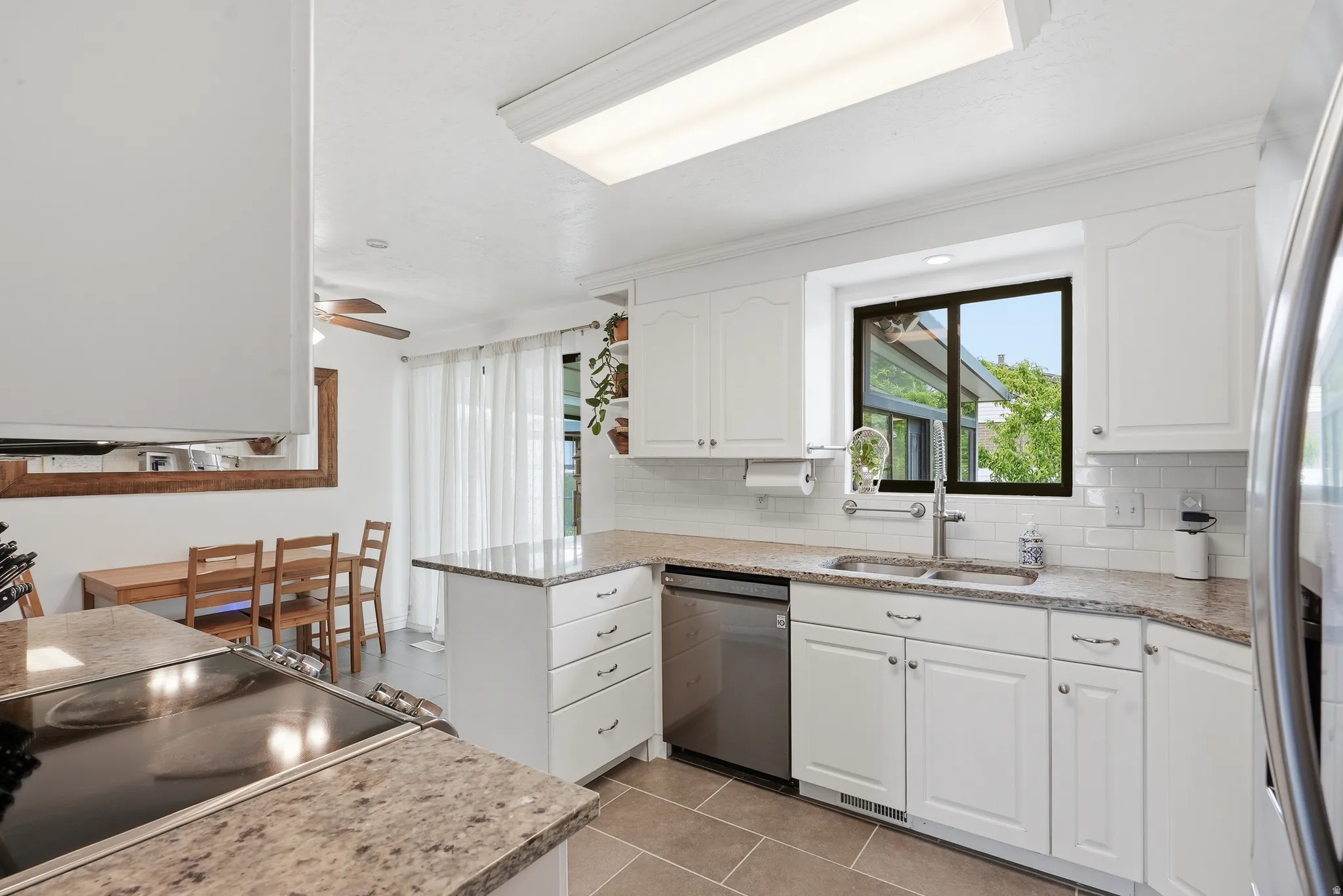 Well-appointed kitchen featuring white cabinetry, light granite countertops, subway tile backsplash, stainless steel dishwasher, and a window above the sink