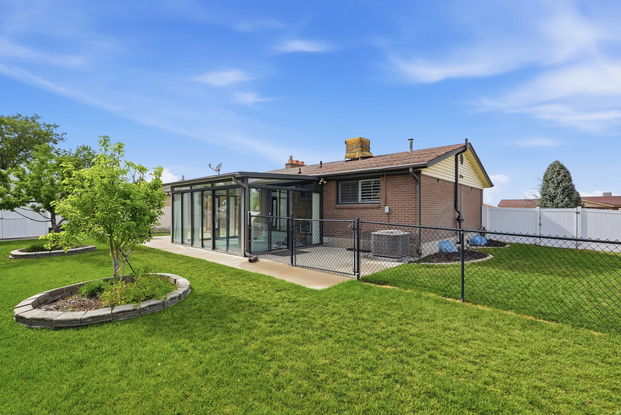Expansive backyard featuring a manicured lawn, a detached sunroom with full-height glass panels, a concrete patio, and mature trees with stone-edged planters