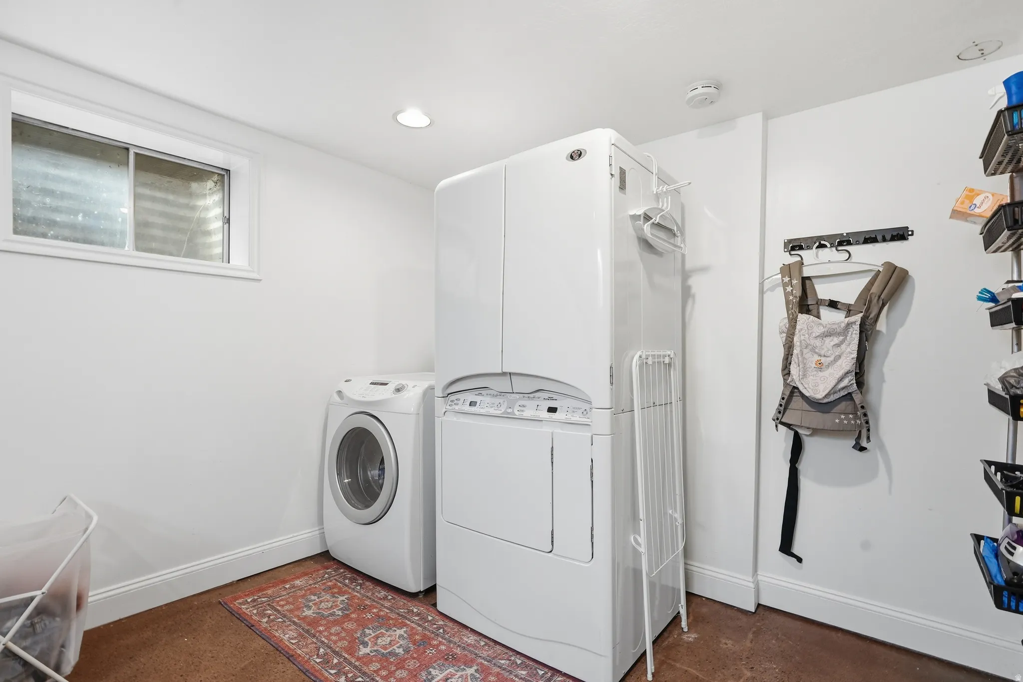 Dedicated laundry area featuring a front-loading washing machine, stacked dryer unit, and a window