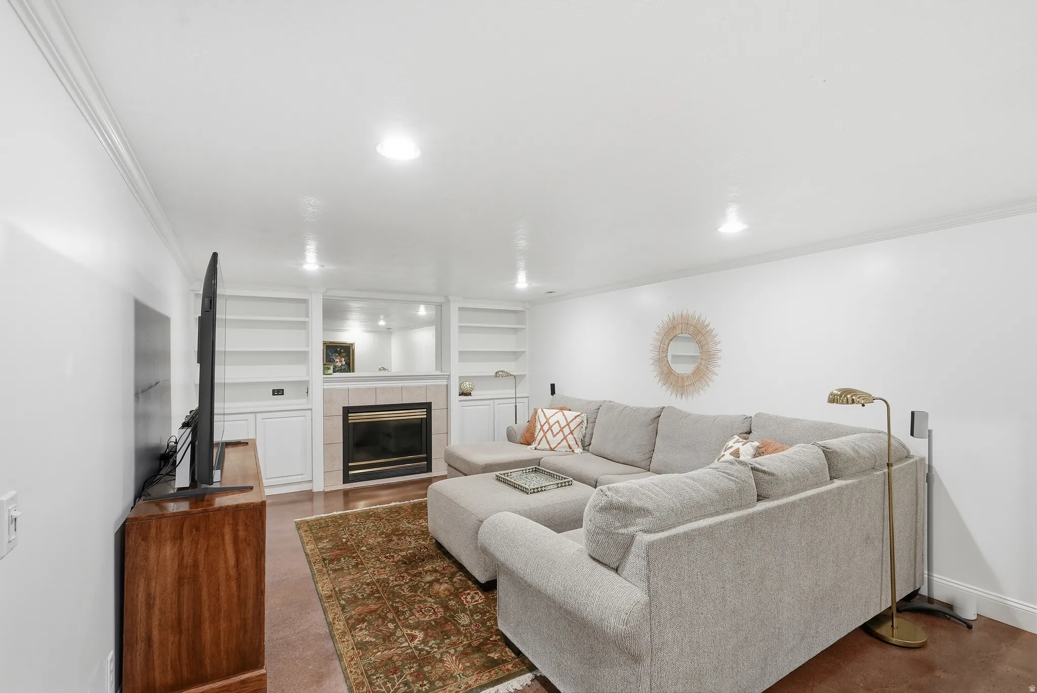 Living area featuring a central fireplace with a tiled surround, built-in shelving, crown molding, recessed lighting, and wood-finish flooring