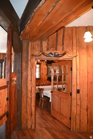 Rustic wood-paneled interior featuring exposed wood beams, wood-finish flooring, and a solid wood door with glass paneling
