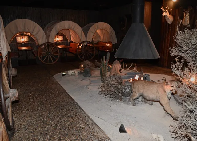 Interior space featuring a desert-themed display with multiple covered wagons, a freestanding conical fireplace, and a simulated sandy terrain