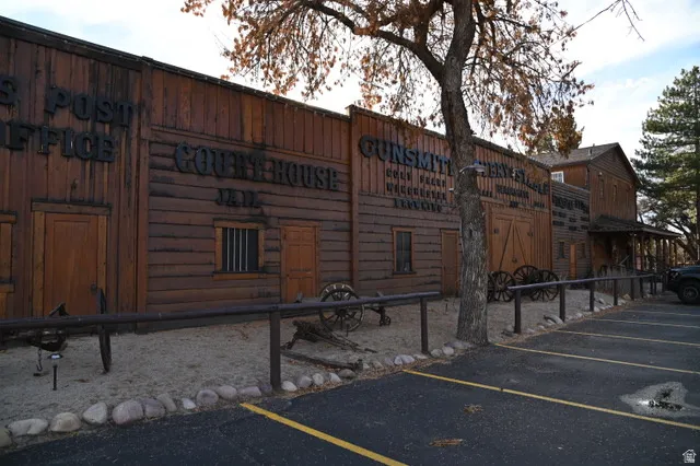 Rustic wood-clad facade featuring multiple storefronts with distinct signage, a gravel perimeter, and a paved parking area