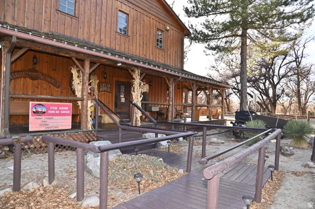 Exterior featuring a rustic wood-plank facade, a covered porch with log-style supports, dark wood-finish decking, an accessible ramp with railings, and established landscaping with mature trees