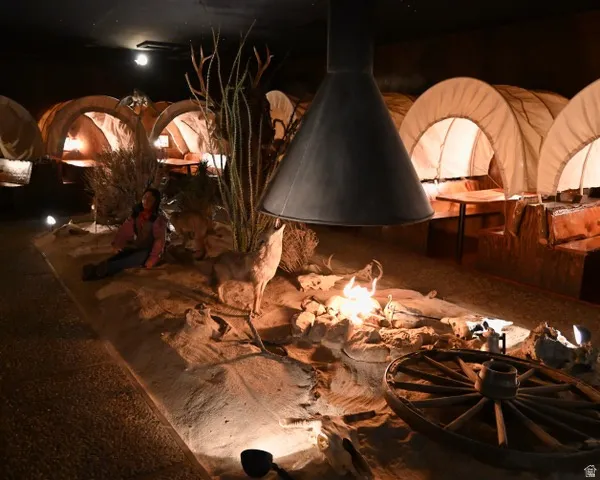 Thematic interior space featuring multiple covered wagon structures, a central display with simulated desert landscaping, an overhead metal hood, and integrated lighting