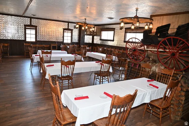 Spacious dining area featuring wood-finish flooring, pressed tin wall panels, a wagon wheel chandelier, multiple windows, and a decorative wagon display