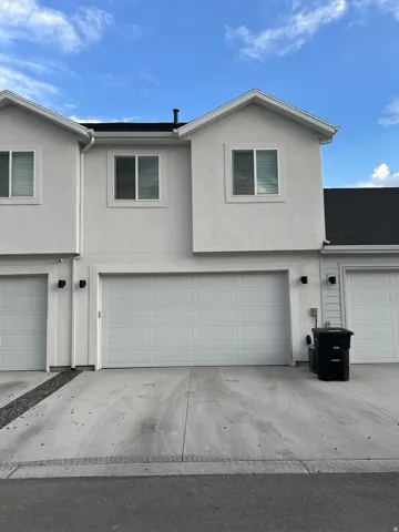 Stucco exterior with a pitched roofline, featuring two attached garage doors, concrete driveways, and upper-level windows