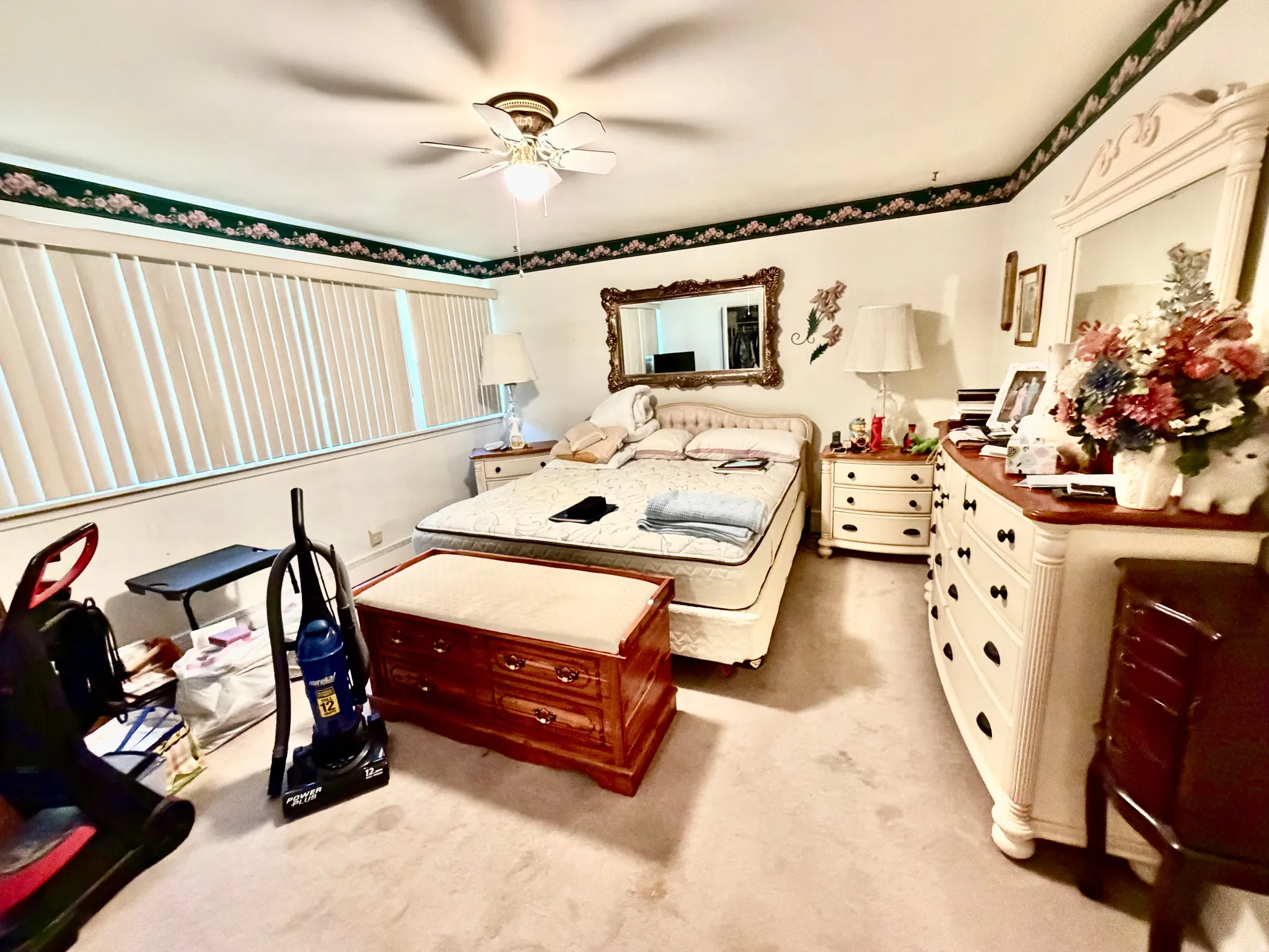 Spacious room featuring broad windows with vertical blinds, ceiling fan, and carpeted flooring
