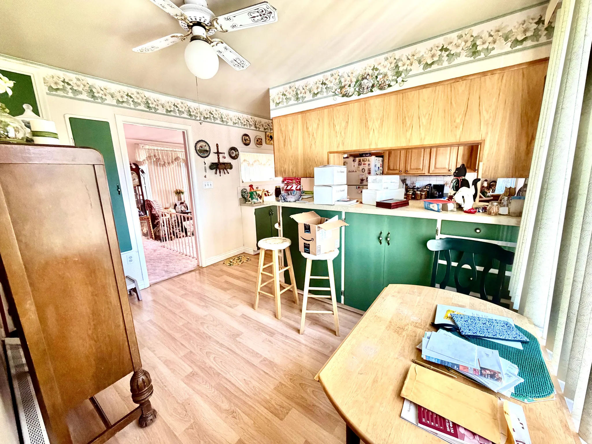Kitchen featuring wood-finish flooring, a ceiling fan with light fixture, wood-paneled walls, and green base cabinetry with light wood upper cabinets