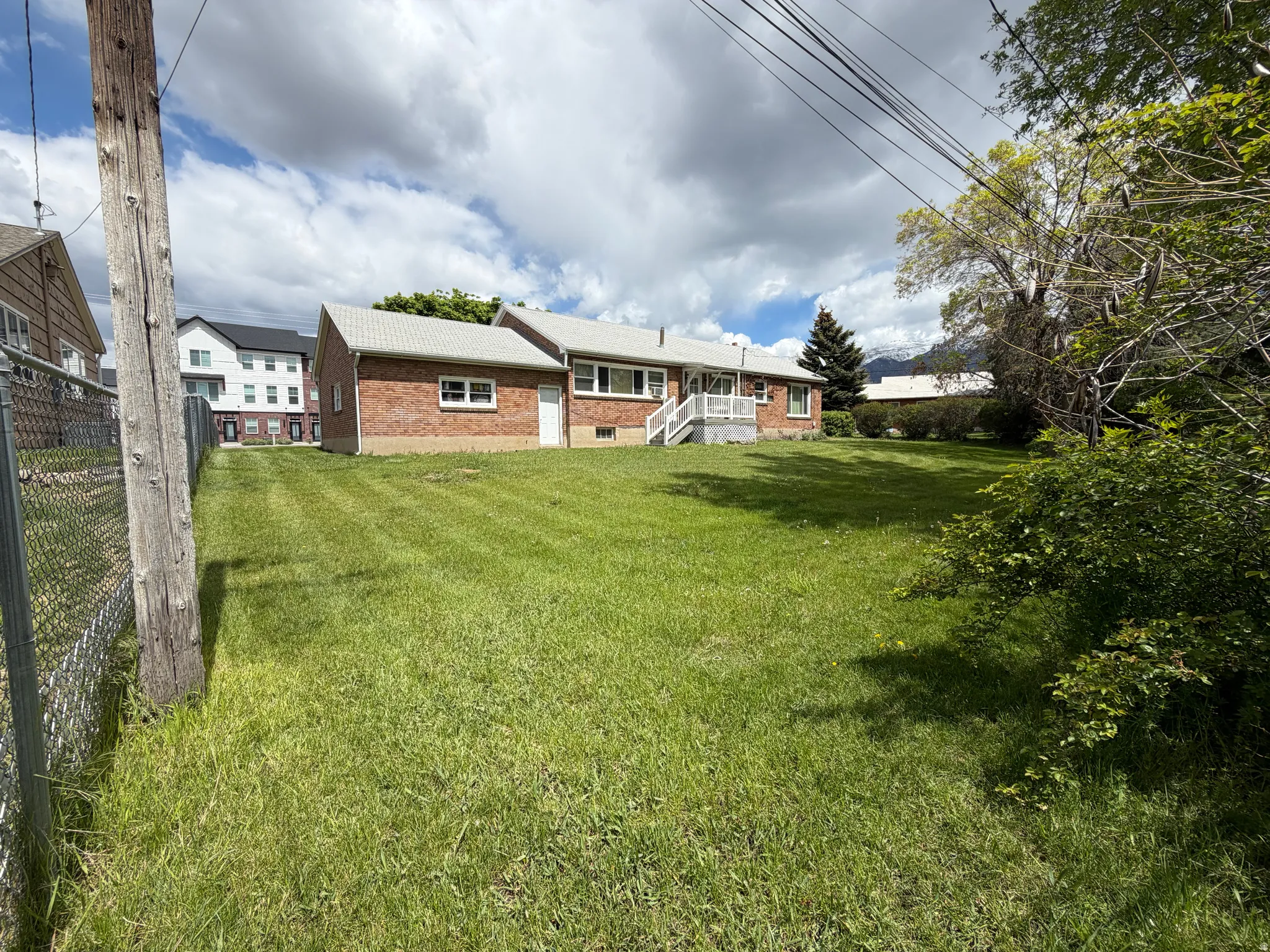 Expansive green lawn with mature trees and a brick exterior residence featuring multiple windows and a white deck