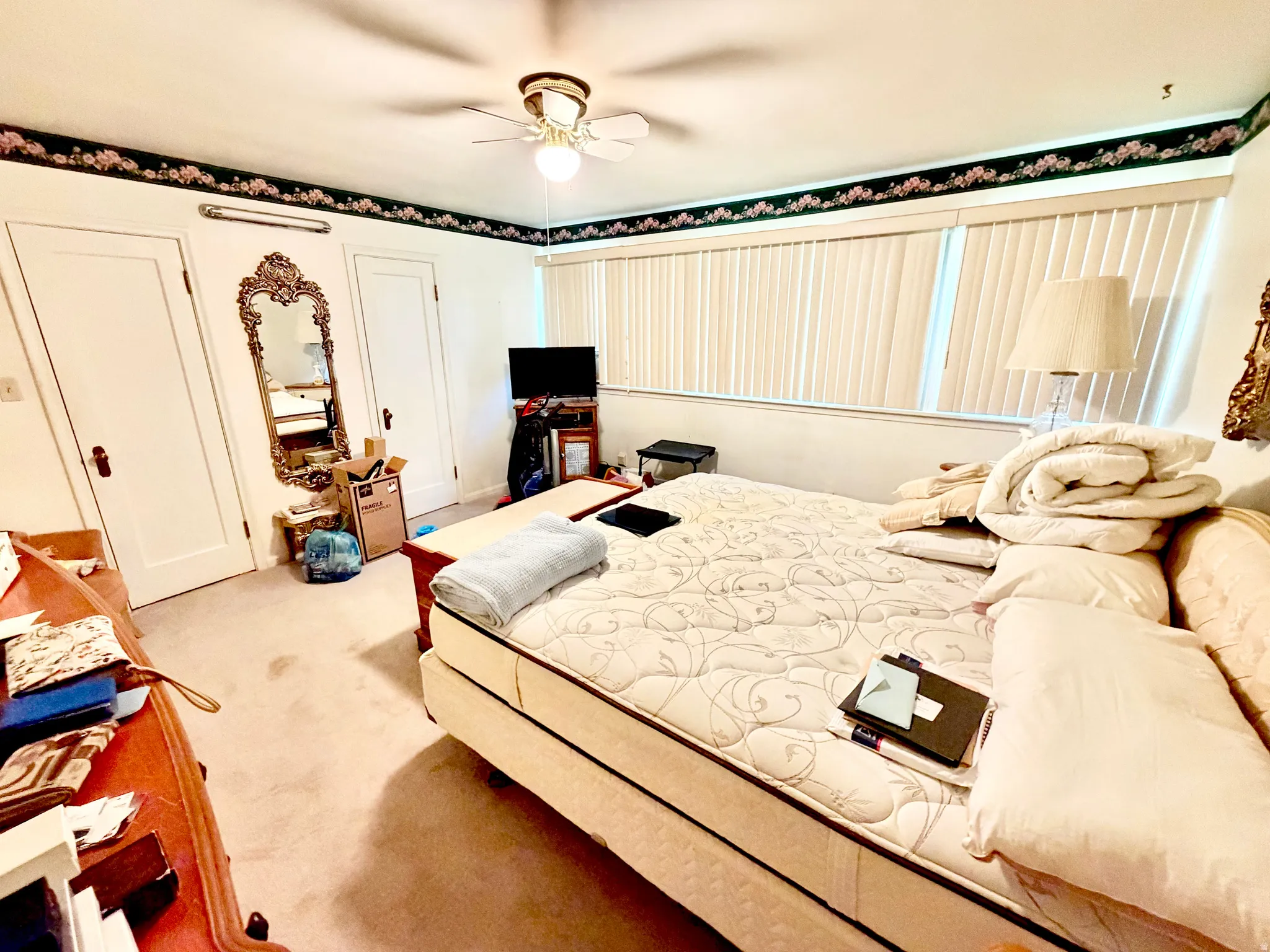 Carpeted room featuring a ceiling fan with integrated lighting, multiple windows with vertical blinds, and two paneled doors with dark hardware