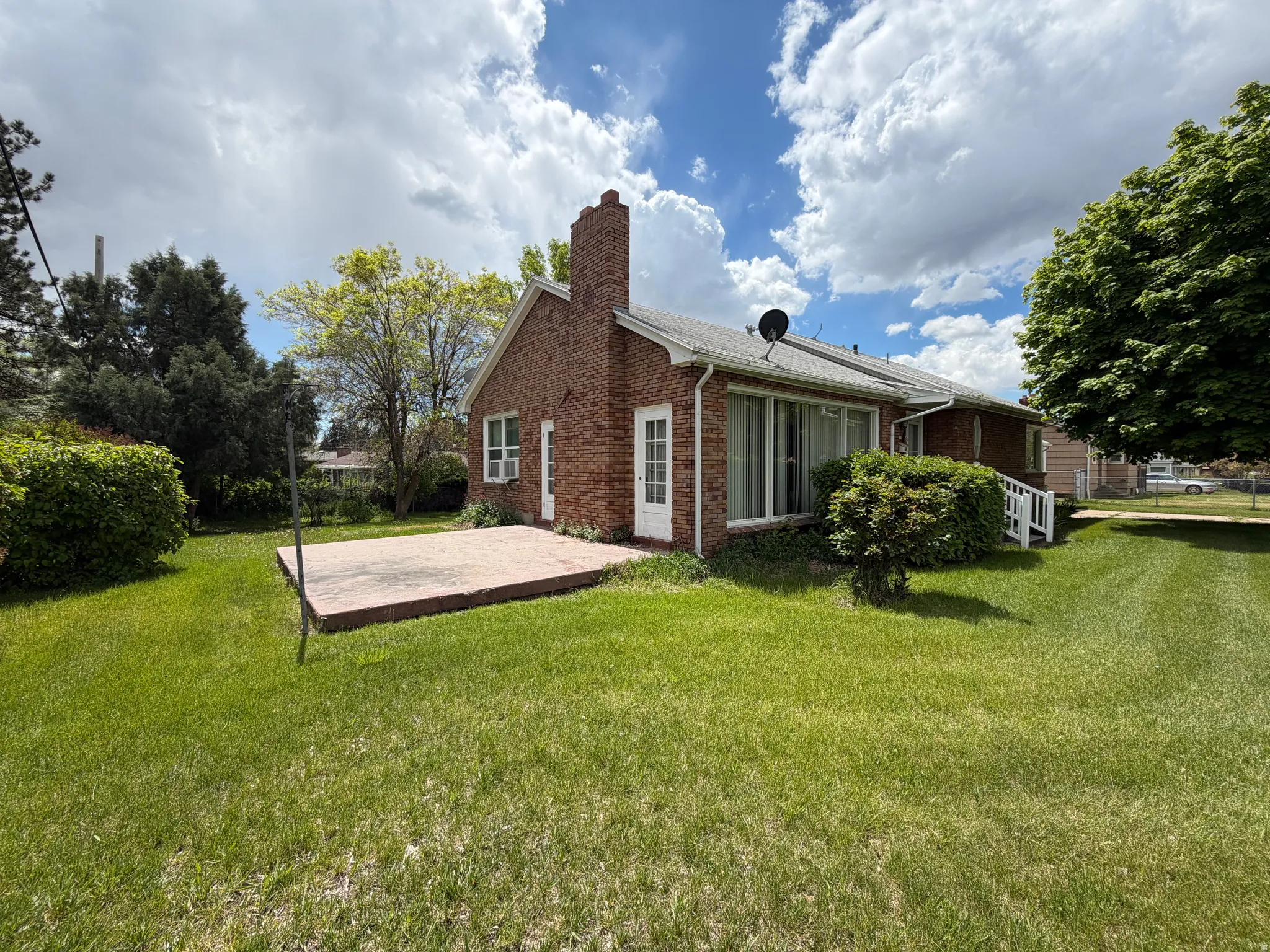 Expansive grassy yard with mature trees, a brick exterior, a concrete patio, and a white entry door