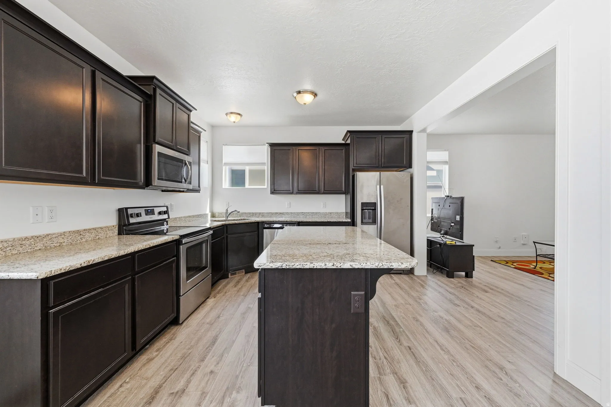 Kitchen with dark wood finish cabinetry, stainless steel appliances, light wood finished floors, and a center island
