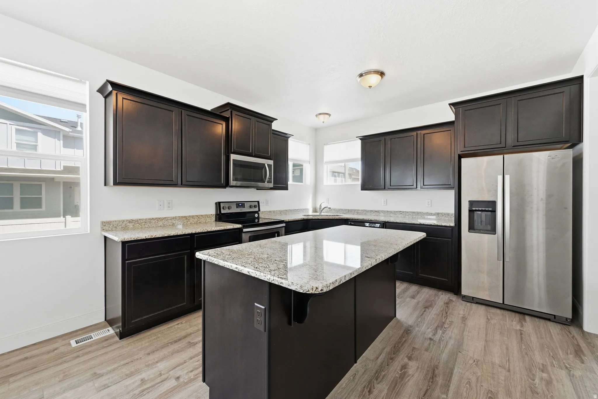 Kitchen with stainless steel appliances, light stone countertops, light wood finished floors, a kitchen island, and dark wood finish cabinets