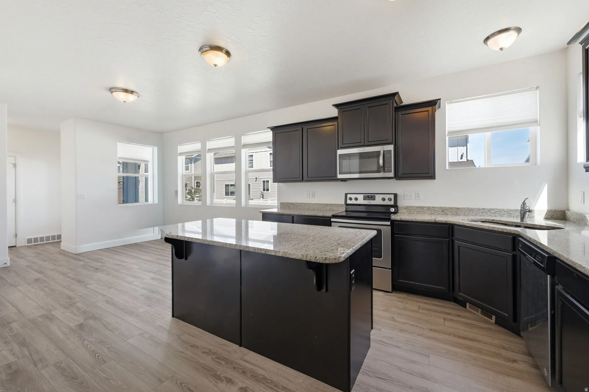 Kitchen featuring light stone counters, stainless steel appliances, a kitchen island, and light wood-style floors