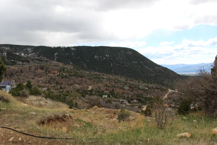 Expansive mountain landscape featuring a distant valley, scattered residences, and diverse tree coverage