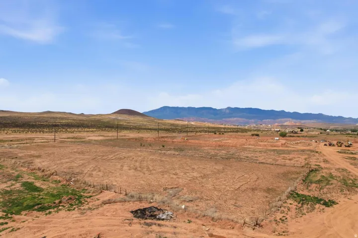 Expansive undeveloped land featuring a dirt road, partial fencing, and distant mountain topography under a clear sky