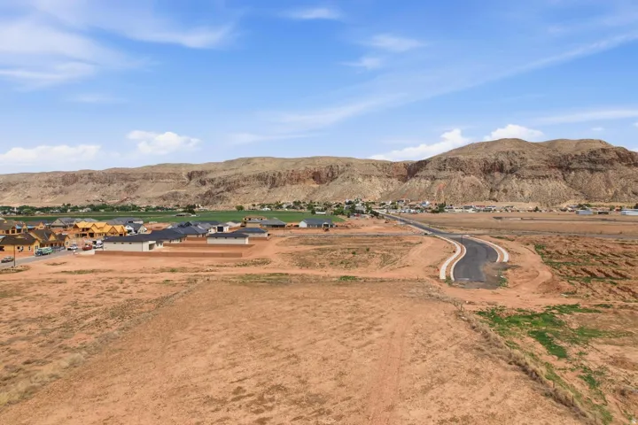 Developing residential community featuring new construction homes with dark roofing, a paved street, and unpaved land plots with a mountain backdrop