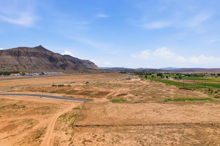 Expansive undeveloped land featuring a paved road, mountain backdrop, and distant green fields