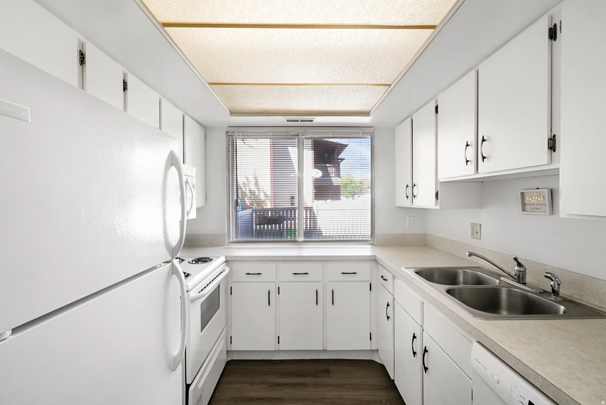 Galley kitchen featuring white cabinetry, light-toned countertops, a double basin stainless steel sink, and wood-finish flooring