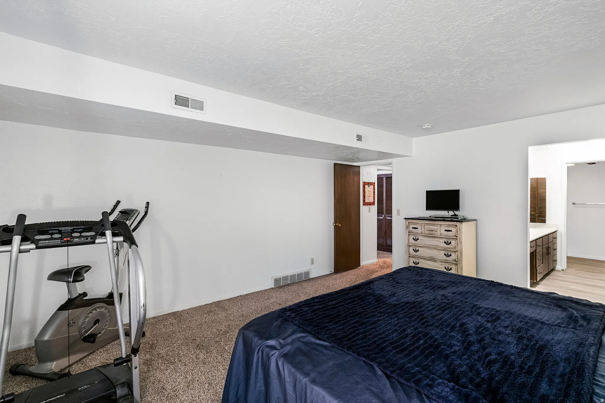 Carpeted room with white walls, a wood-finish door, and baseboard heating